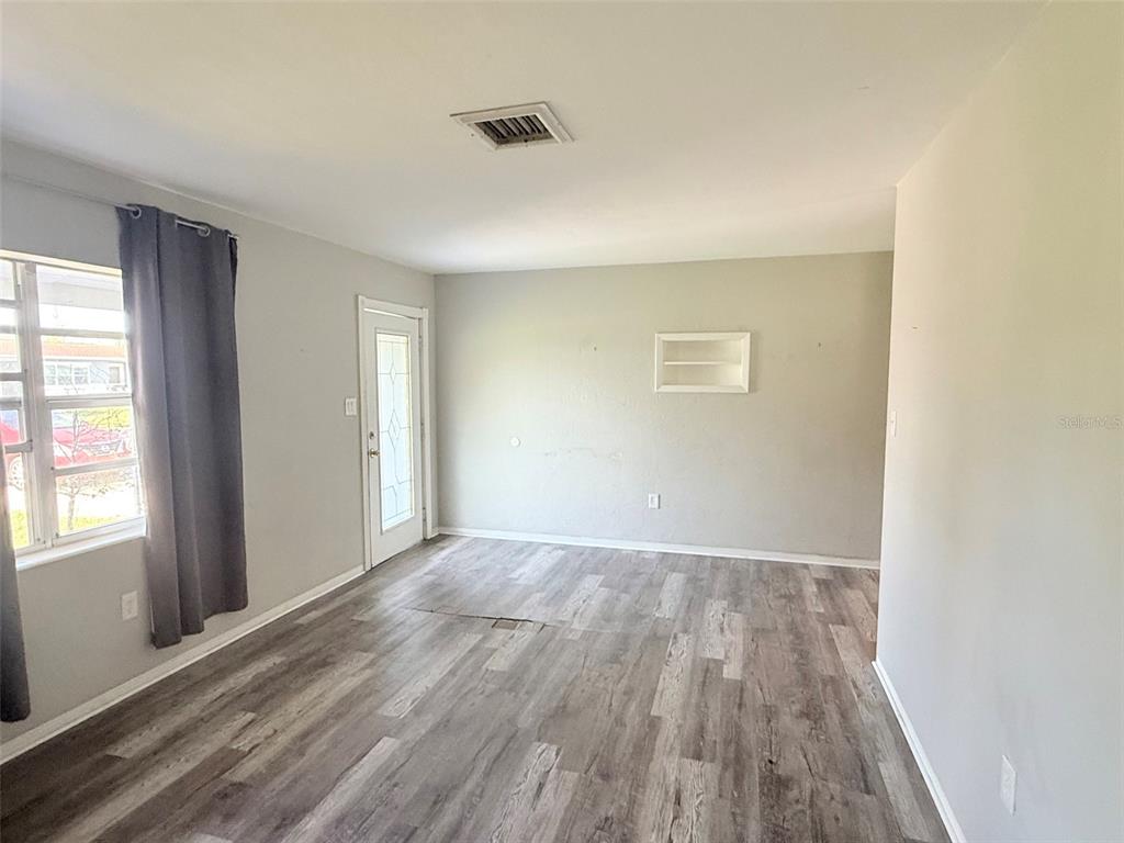 A living room with gray walls, wood-look flooring, a window with curtains, and a door — 6041 43RD AVENUE N, ST PETERSBURG, FL
