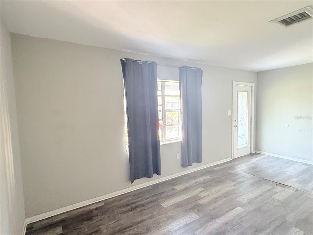 A room with light gray walls, wood-look flooring, a window with dark curtains, and a door — 6041 43RD AVENUE N, ST PETERSBURG, FL