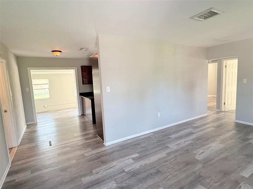 An interior view shows a living area with gray wood-look flooring and a kitchen beyond — 6041 43RD AVENUE N, ST PETERSBURG, FL