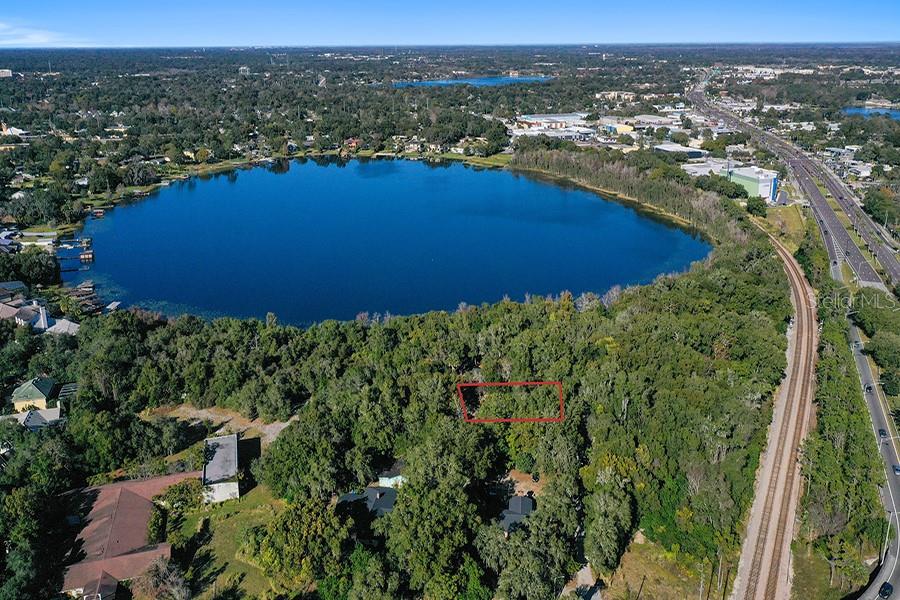 An aerial view shows a wooded lot outlined in red near a lake and railroad tracks — 1130 MECHANIC STREET, MAITLAND, FL