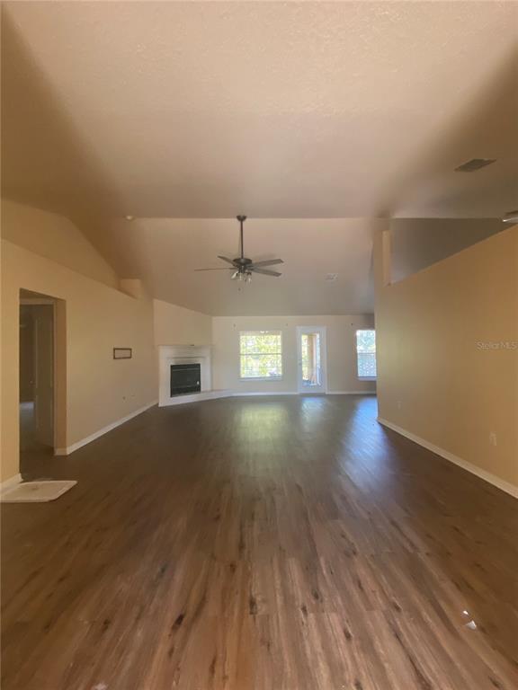 A spacious living room features vaulted ceilings, wood-look flooring, and a corner fireplace — 6775 HIGHLANDS CREEK LOOP, LAKELAND, FL