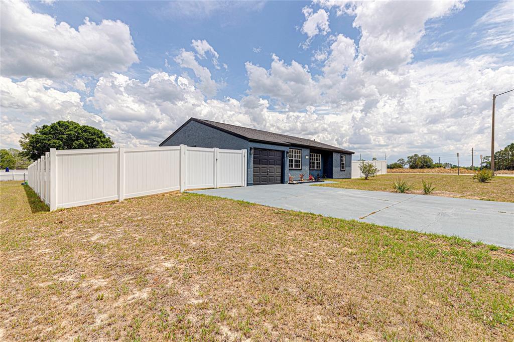 A blue house with a garage and white vinyl fence sits on a grassy lot — 336 OAK TRACK DRIVE, OCALA, FL