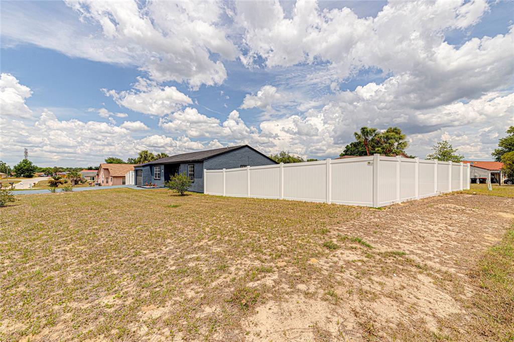 A dark-painted house with a white vinyl fence stands on a large, sandy grass lot — 336 OAK TRACK DRIVE, OCALA, FL