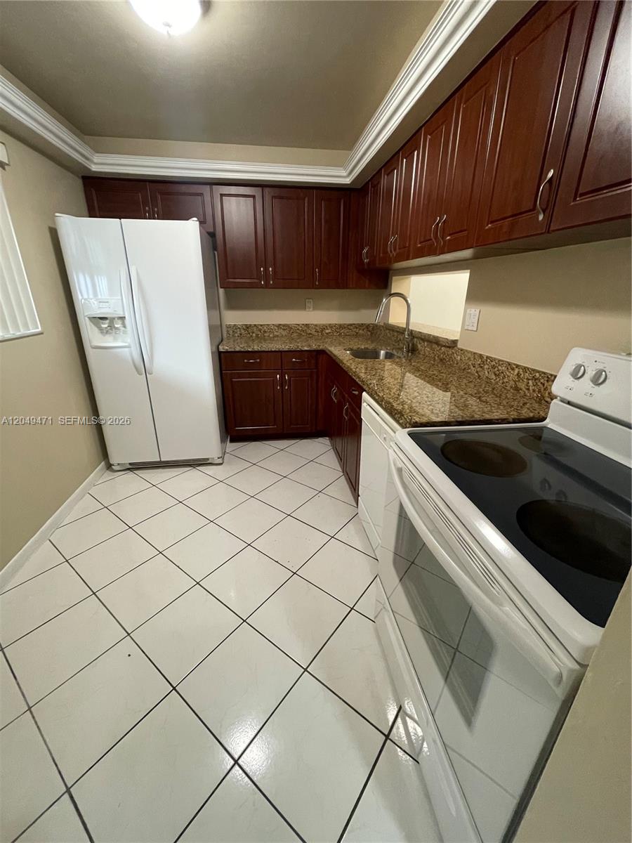 A kitchen features dark wood cabinets, granite countertops, white appliances, and white tiled flooring — 8400 SW 133rd Ave Rd # 424, Miami FL 33183, MIAMI, FL