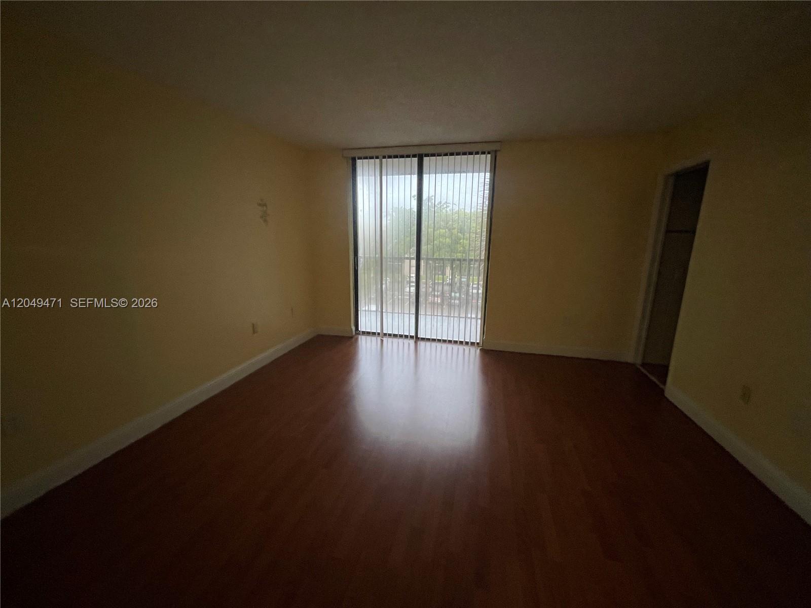 An empty room features light-colored walls, wood-look flooring, and a sliding glass door leading outside — 8400 SW 133rd Ave Rd # 424, Miami FL 33183, MIAMI, FL