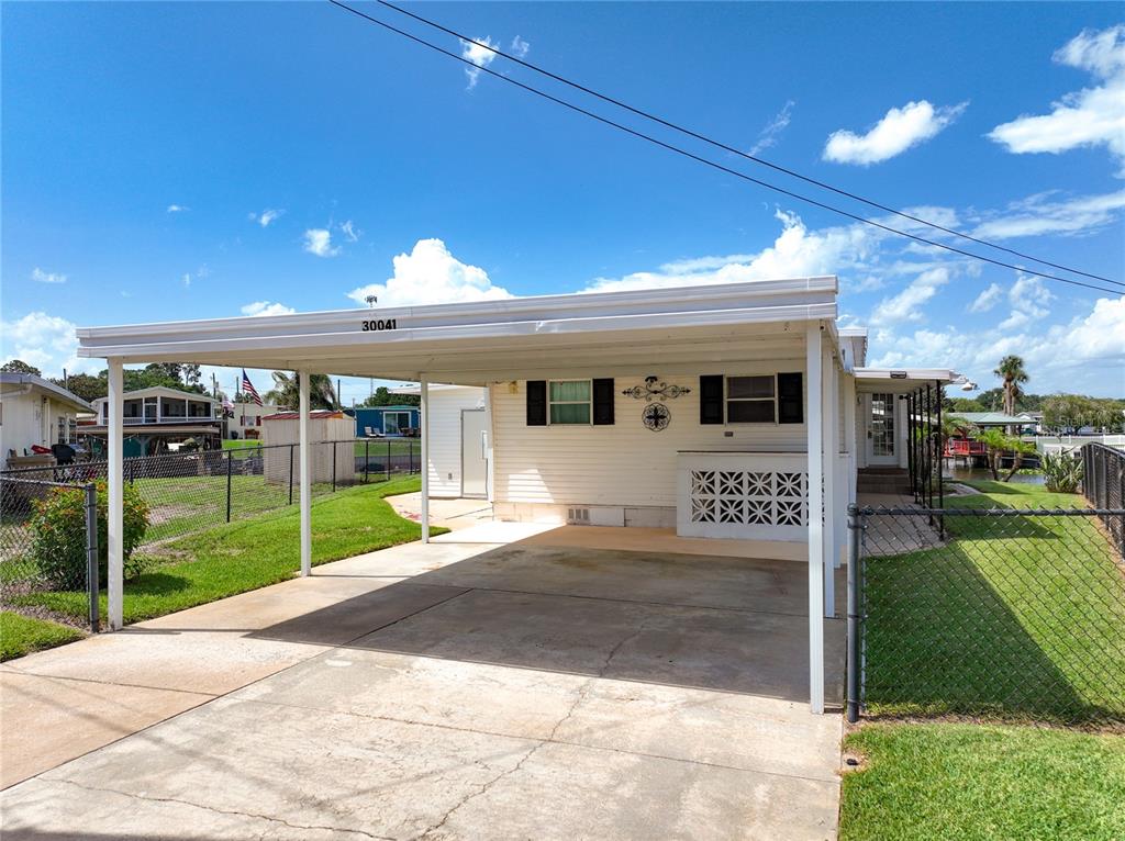 A white mobile home features a concrete carport and a chain-link fenced yard — 30041 WAUSAUKEE DRIVE, TAVARES, FL
