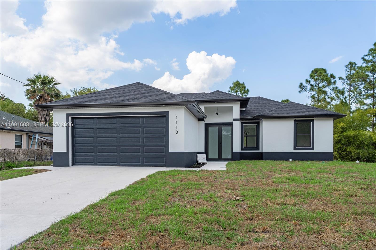 A single-story house with a dark gray garage door, white stucco walls, and dark trim — 1113 ENRIQUE ST E, Lehigh Acres FL 33974, LEHIGH ACRES, FL