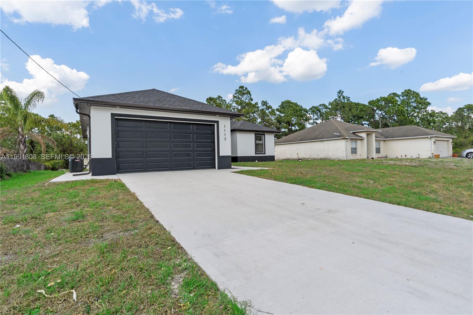 A single-story house with a black garage door and white exterior sits on a lot — 1113 ENRIQUE ST E, Lehigh Acres FL 33974, LEHIGH ACRES, FL