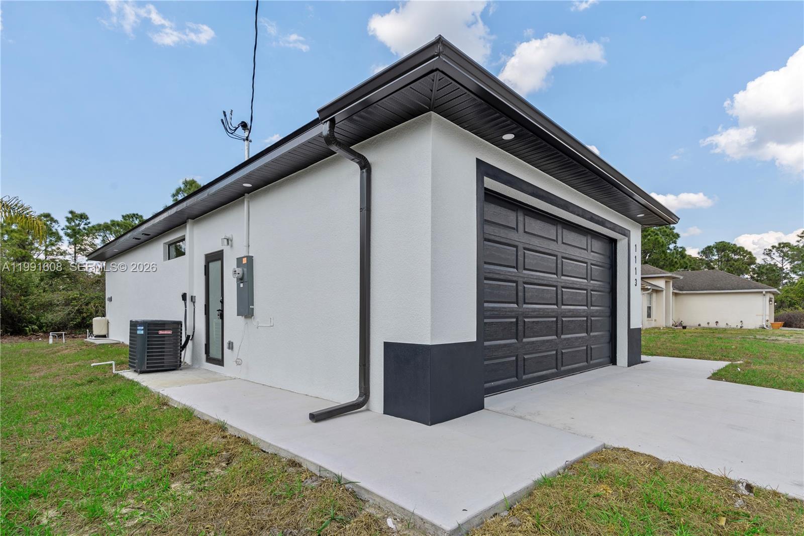 The exterior of a detached garage features white stucco walls, a dark door, and trim — 1113 ENRIQUE ST E, Lehigh Acres FL 33974, LEHIGH ACRES, FL