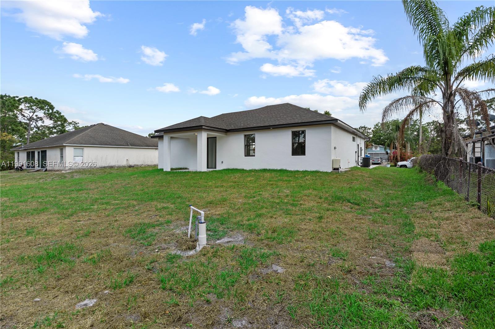 The rear exterior of a white single-story house features a covered patio and a well pump — 1113 ENRIQUE ST E, Lehigh Acres FL 33974, LEHIGH ACRES, FL