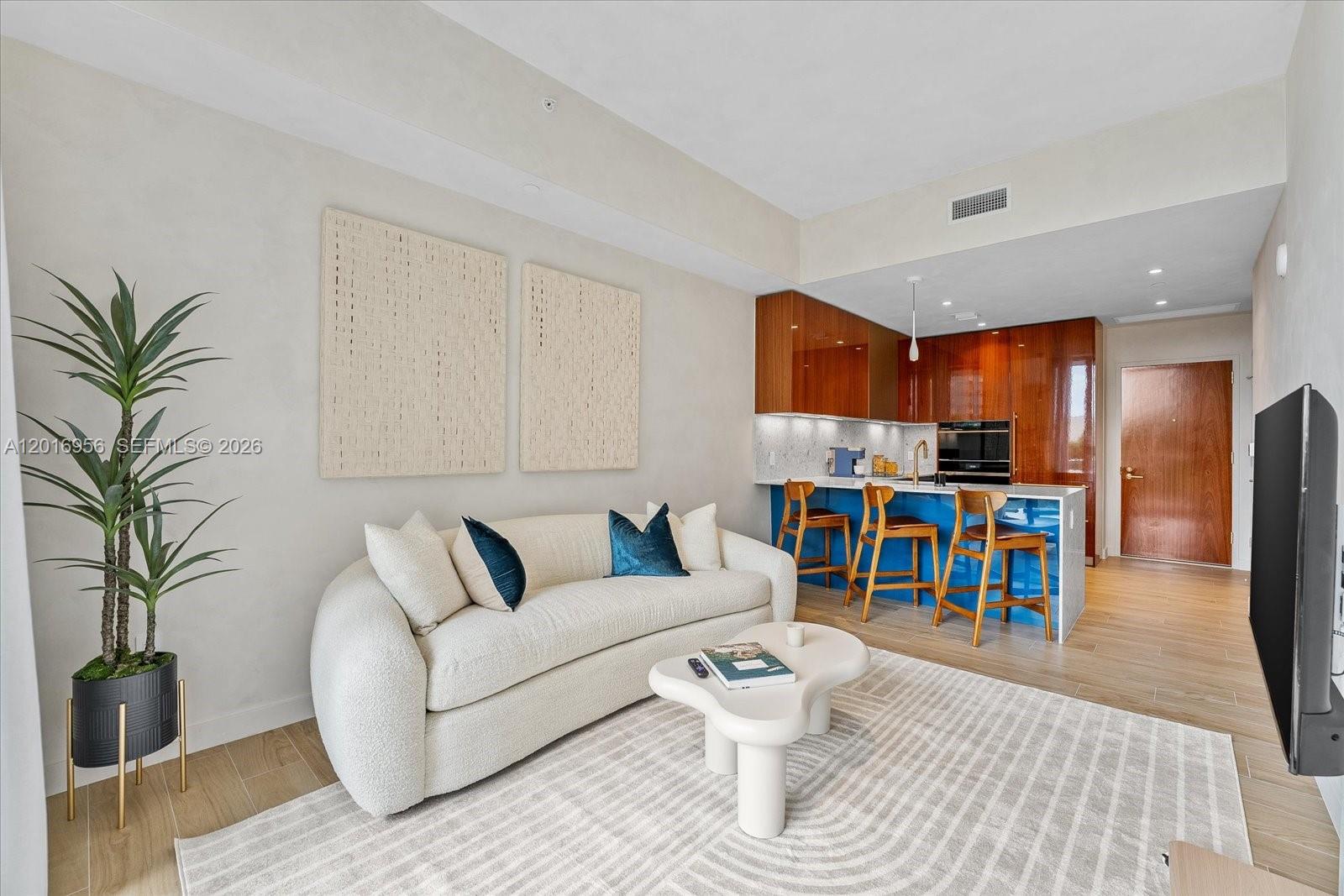 A living room features a curved white sofa, a coffee table, and an open kitchen — 2678 Tigertail Ave # 315, Miami FL 33133, MIAMI, FL