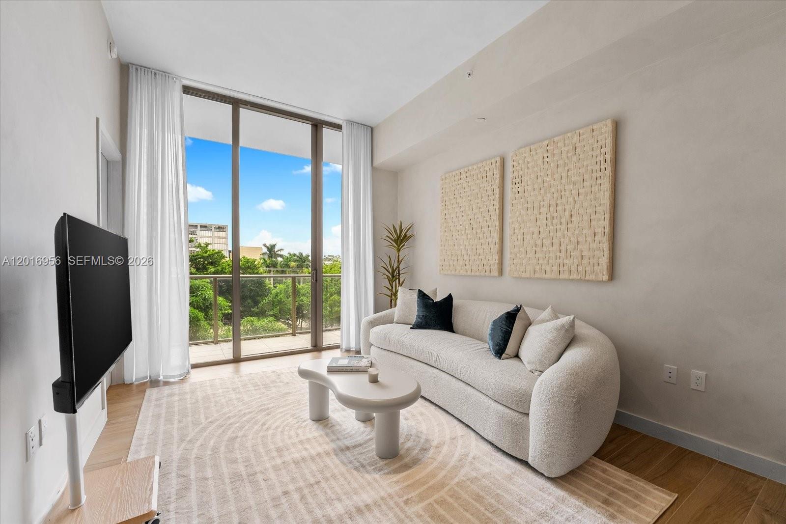 A modern living room features a curved sofa, a coffee table, and floor-to-ceiling windows — 2678 Tigertail Ave # 315, Miami FL 33133, MIAMI, FL