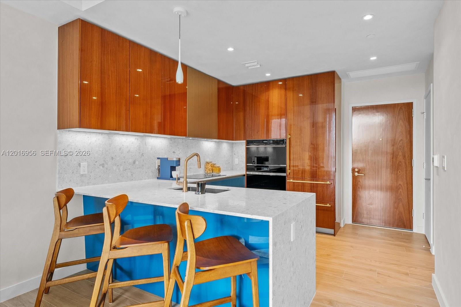 A modern kitchen features wood-veneer cabinetry, a blue island base, and white stone countertops — 2678 Tigertail Ave # 315, Miami FL 33133, MIAMI, FL
