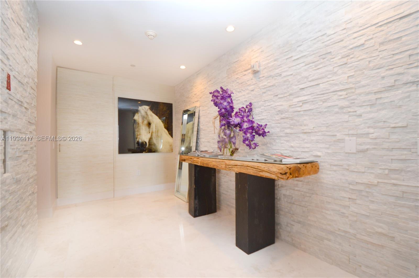 A hallway features a textured stone wall, a rustic wooden console table, and horse artwork — 1100 Biscayne Blvd # 6104, Miami FL 33132, MIAMI, FL