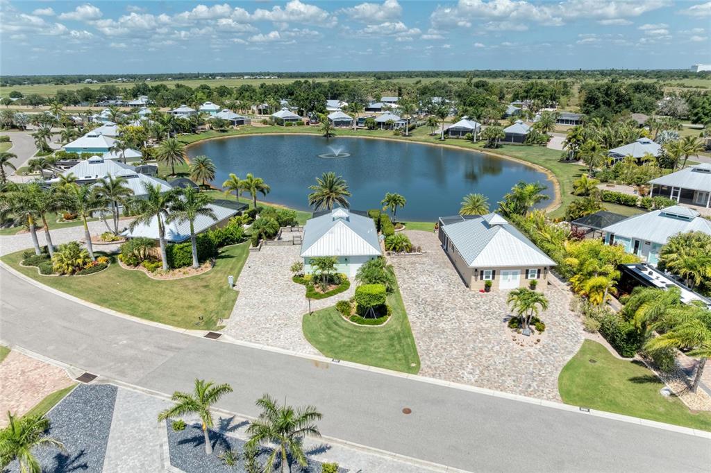 An aerial view shows two houses with metal roofs situated along a pond with fountains — 8153 SW BIMINI WAY LOT 30, ARCADIA, FL