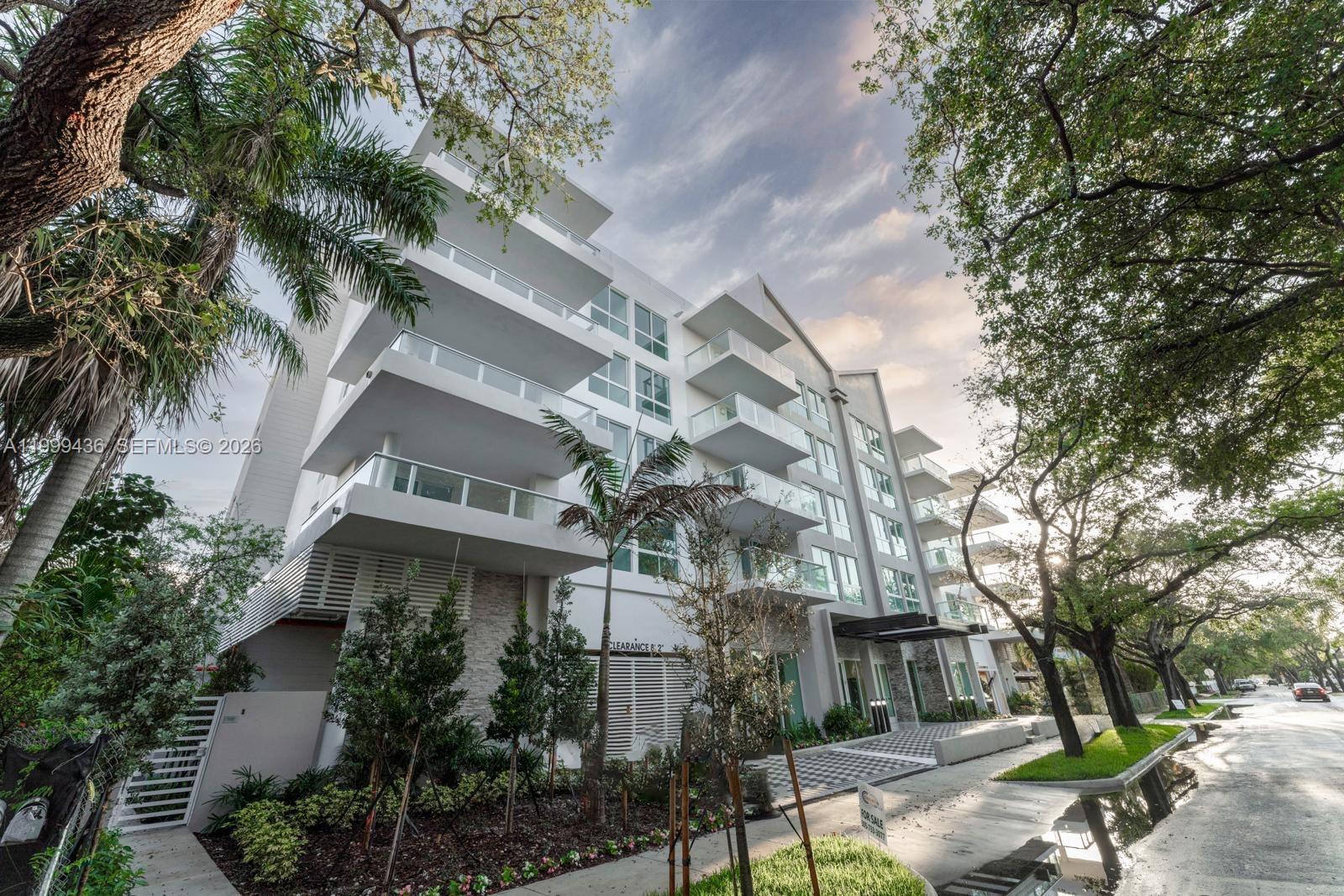 A modern multi-story apartment building with glass balconies stands beside a tree-lined street — 1850 Monroe St # 409, Hollywood FL 33020, HOLLYWOOD, FL