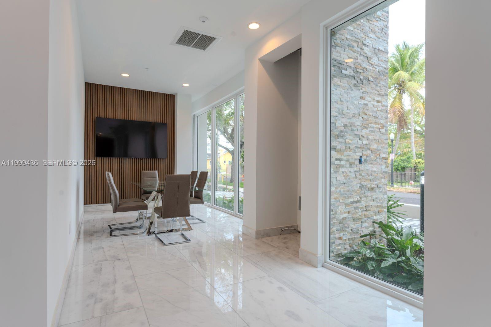 A dining area features a slatted wood accent wall, glass table, and floor-to-ceiling windows — 1850 Monroe St # 409, Hollywood FL 33020, HOLLYWOOD, FL
