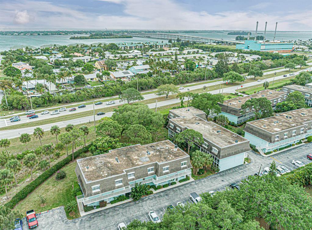 An aerial view shows multi-story apartment buildings with flat roofs surrounded by trees and parking — 1901 Indian River Boulevard # 104C, Vero Beach FL 32960, VERO BEACH, FL