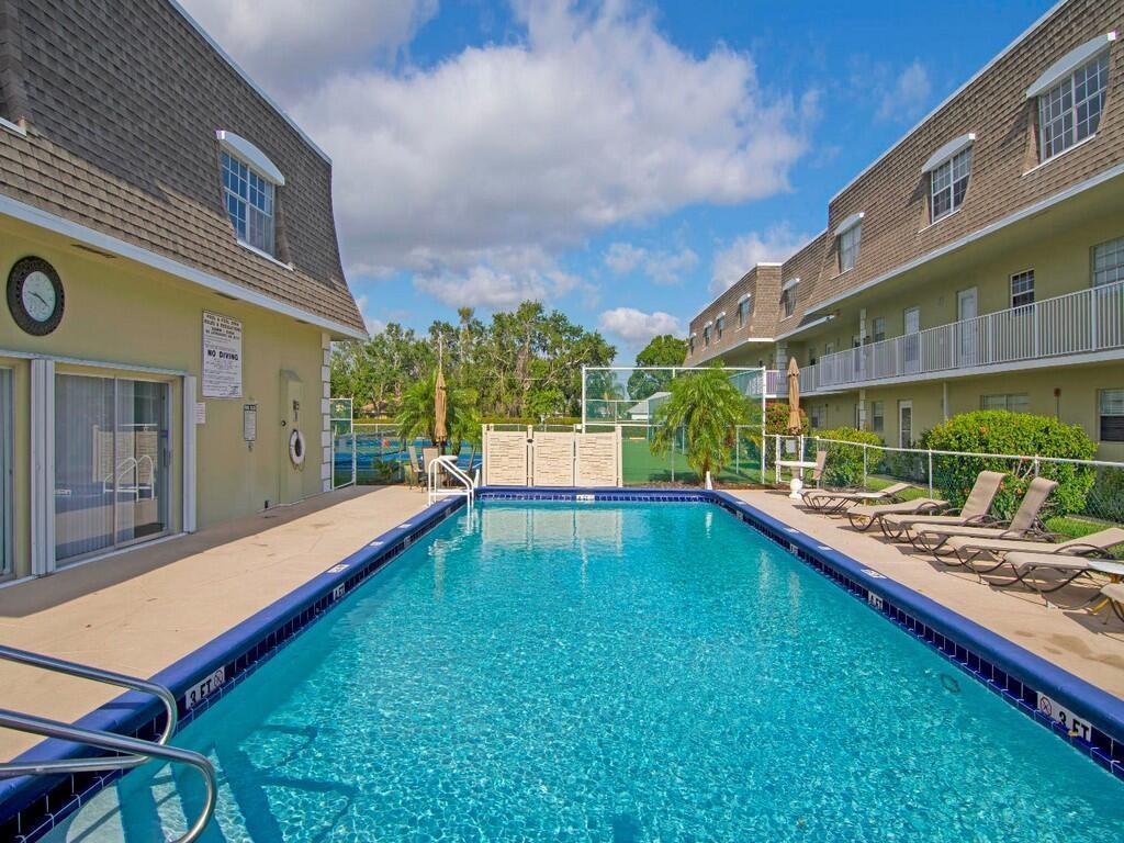 A rectangular swimming pool sits between two multi-story apartment buildings with tan siding — 1901 Indian River Boulevard # 104C, Vero Beach FL 32960, VERO BEACH, FL