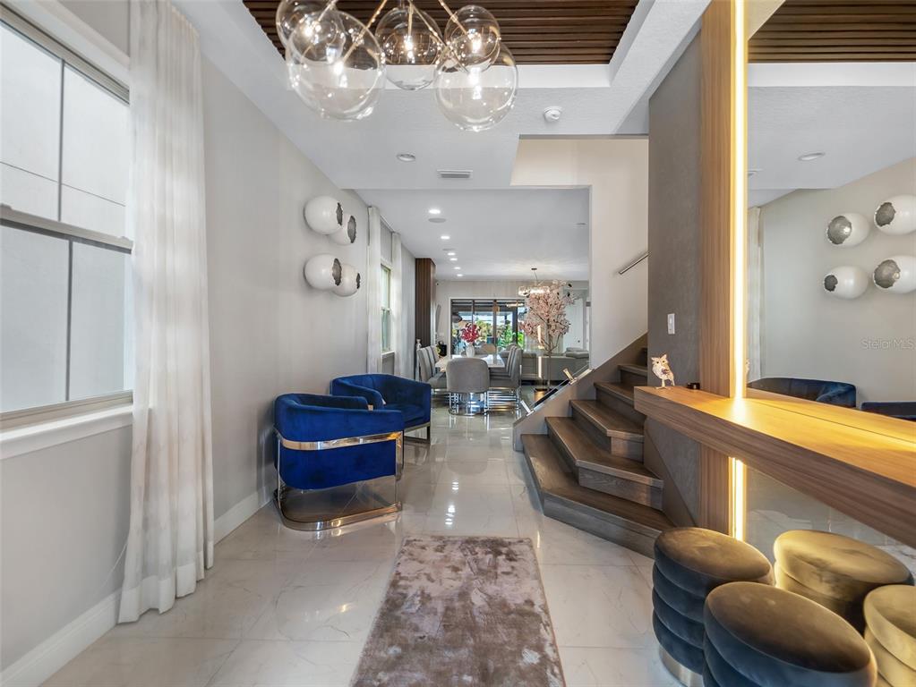 A modern entryway features blue velvet chairs, a wooden staircase, and a contemporary globe chandelier — 13759 LARKTON LANE, ORLANDO, FL