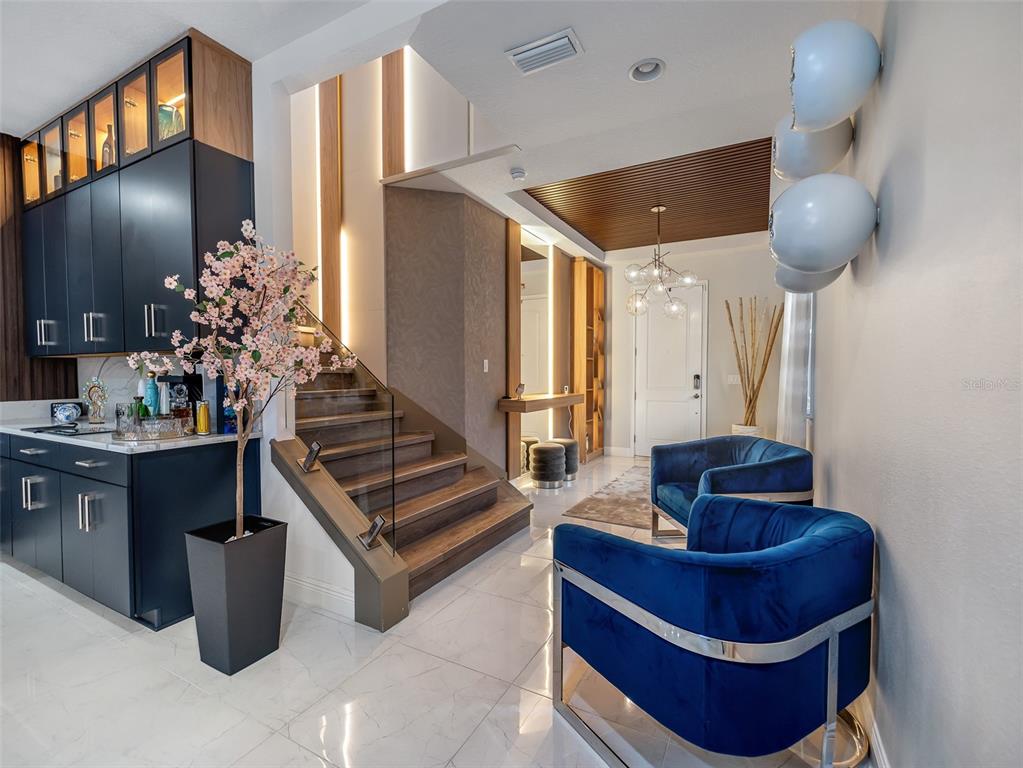 A modern entryway features a staircase, blue velvet chairs, dark cabinetry, and a slatted ceiling — 13759 LARKTON LANE, ORLANDO, FL