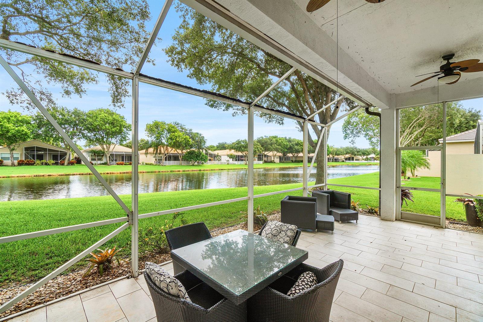 A screened-in patio features a glass-top dining set and overlooks a lake and lawn — 12196 Landrum Way, Boynton Beach FL 33437, BOYNTON BEACH, FL