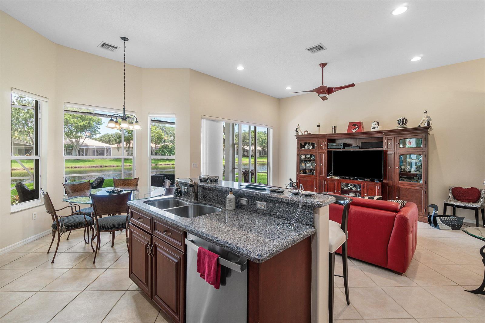 A kitchen with granite countertops and dark wood cabinets overlooks a living room and lake — 12196 Landrum Way, Boynton Beach FL 33437, BOYNTON BEACH, FL