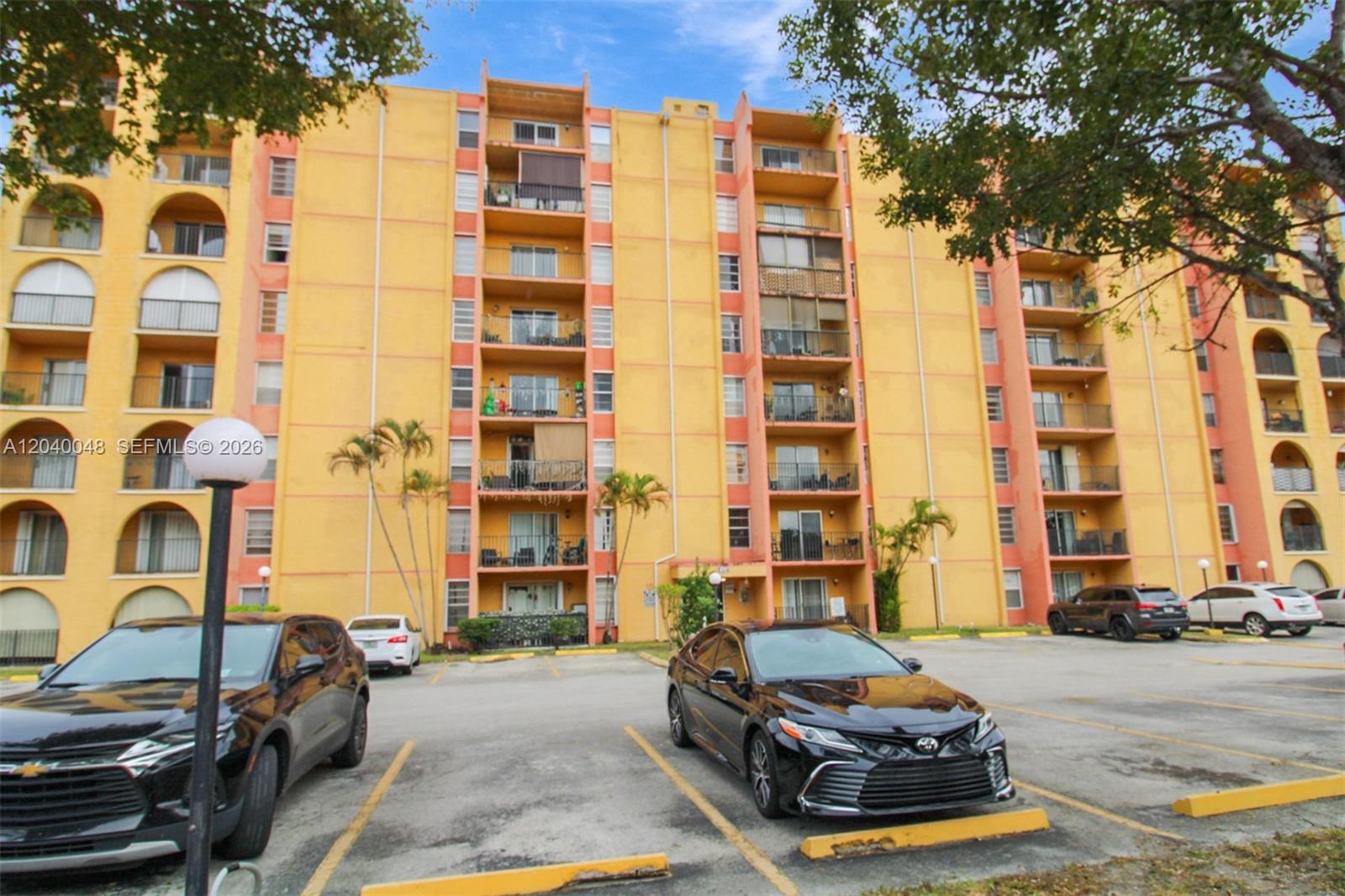 A multi-story yellow apartment building stands behind a parking lot with several parked cars — 4717 NW 7th St # 10, Miami FL 33126, MIAMI, FL