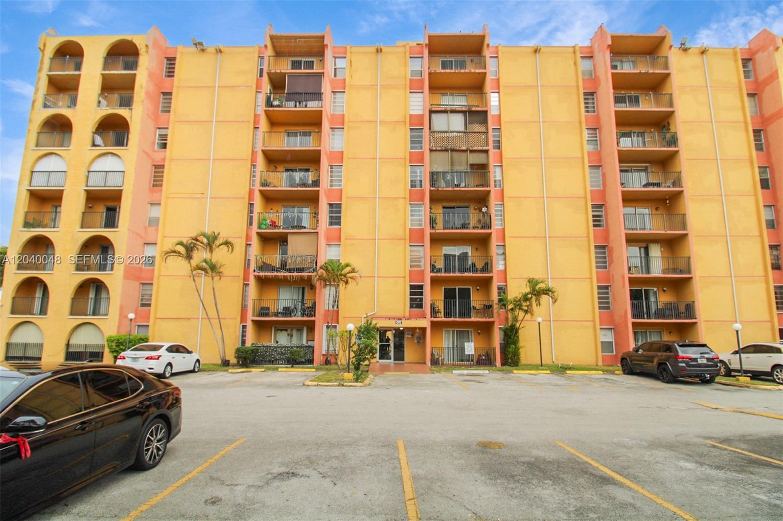 A multi-story yellow apartment building features balconies and a parking lot in the foreground — 4717 NW 7th St # 10, Miami FL 33126, MIAMI, FL