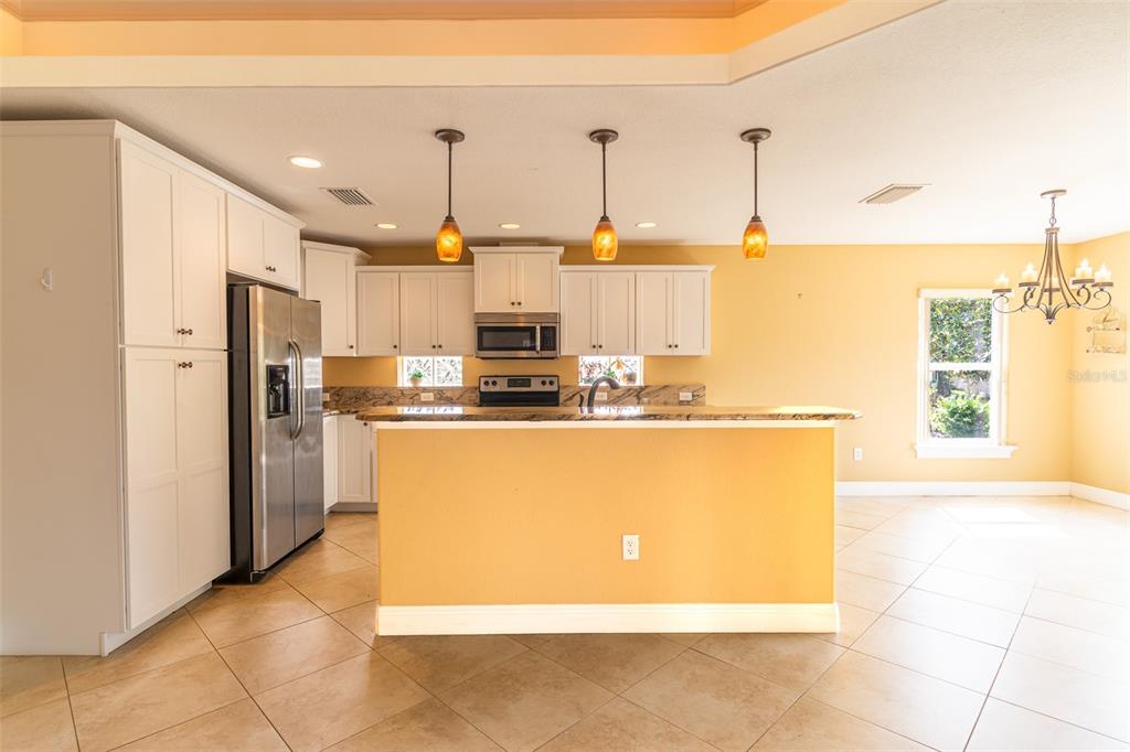 A kitchen with white cabinets, stainless steel appliances, a granite island, and yellow walls — 3715 SEBRING PARKWAY, SEBRING, FL