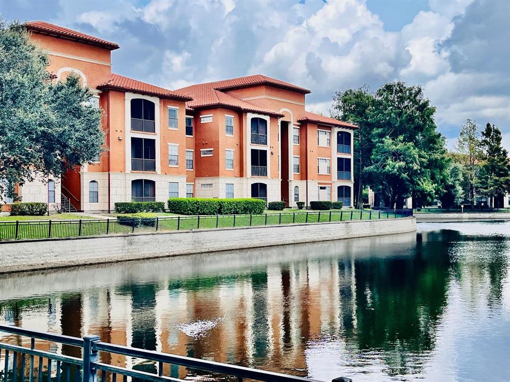A multi-story apartment building with orange stucco walls and a tiled roof overlooks a pond — 6149 METROWEST BOULEVARD UNIT 305, ORLANDO, FL