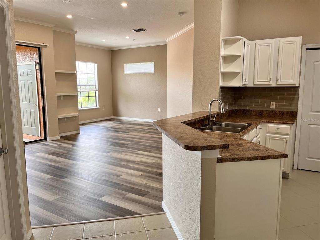 A kitchen with a breakfast bar overlooks a living area with wood-look flooring — 6149 METROWEST BOULEVARD UNIT 305, ORLANDO, FL