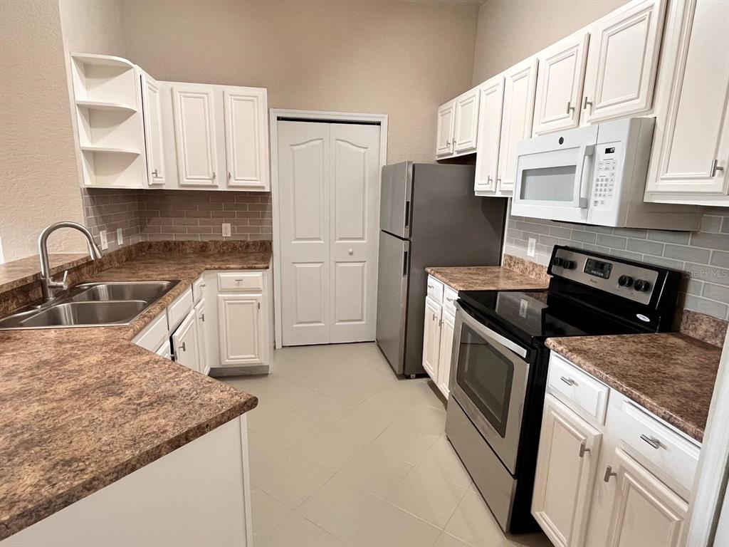 A kitchen features white cabinets, brown laminate countertops, stainless steel appliances, and a tiled backsplash — 6149 METROWEST BOULEVARD UNIT 305, ORLANDO, FL