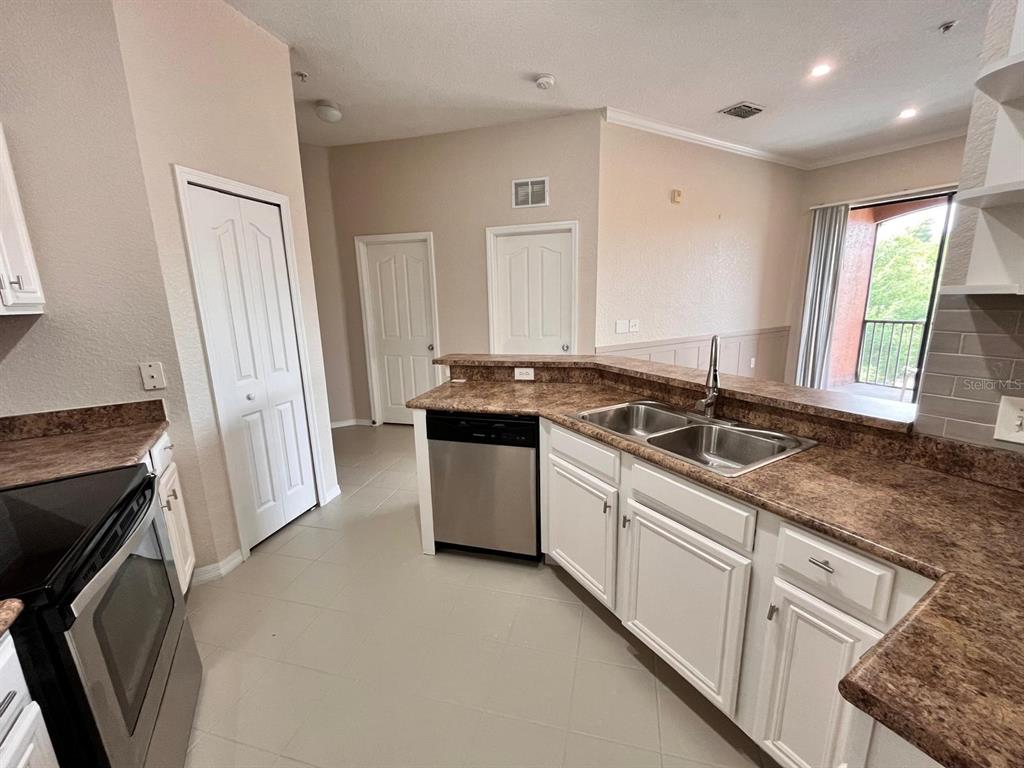 A kitchen with white cabinets, brown laminate countertops, stainless steel appliances, and a balcony view — 6149 METROWEST BOULEVARD UNIT 305, ORLANDO, FL