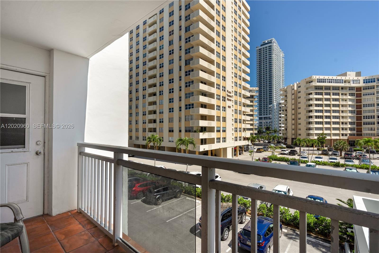A balcony overlooks a parking lot and several high-rise apartment buildings under a clear sky — 1849 S Ocean Dr # 305, Hallandale Beach FL 33009, HALLANDALE BEACH, FL