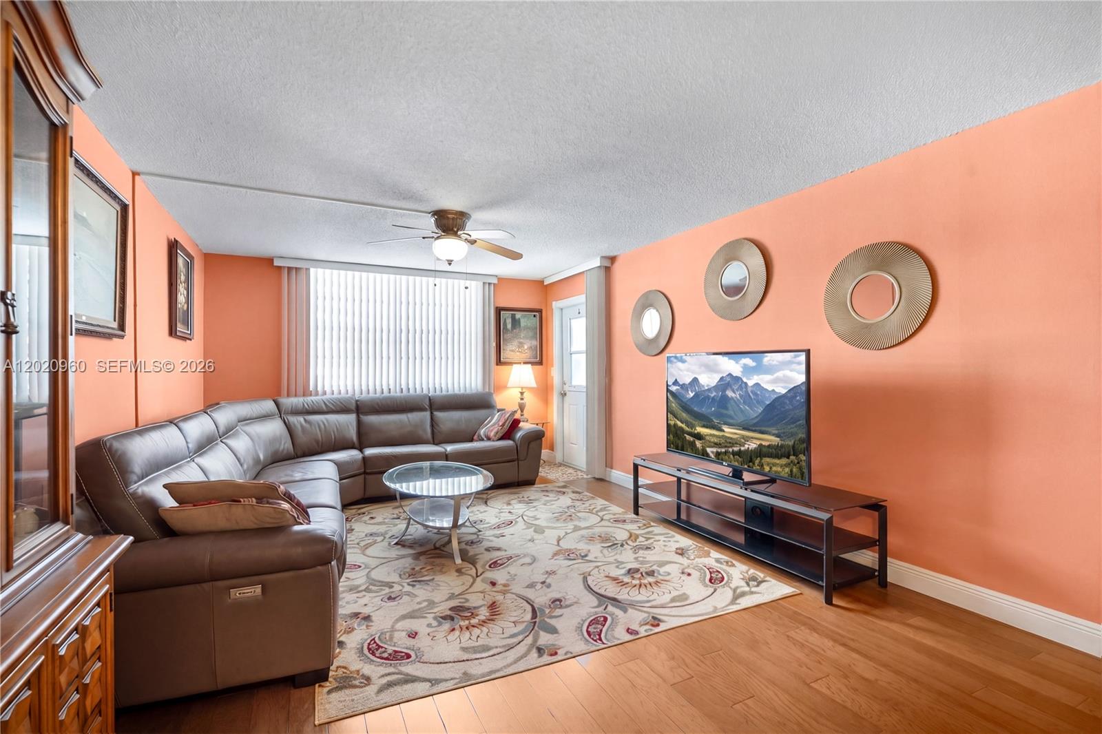A living room features a brown sectional sofa, a television on a stand, and peach walls — 1849 S Ocean Dr # 305, Hallandale Beach FL 33009, HALLANDALE BEACH, FL