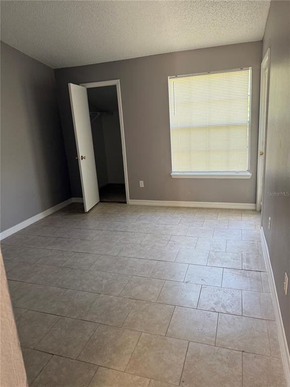An empty bedroom features gray walls, light-colored tile flooring, a window with blinds, and a closet — 1948 LAKE ATRIUMS CIRCLE UNIT 133, ORLANDO, FL