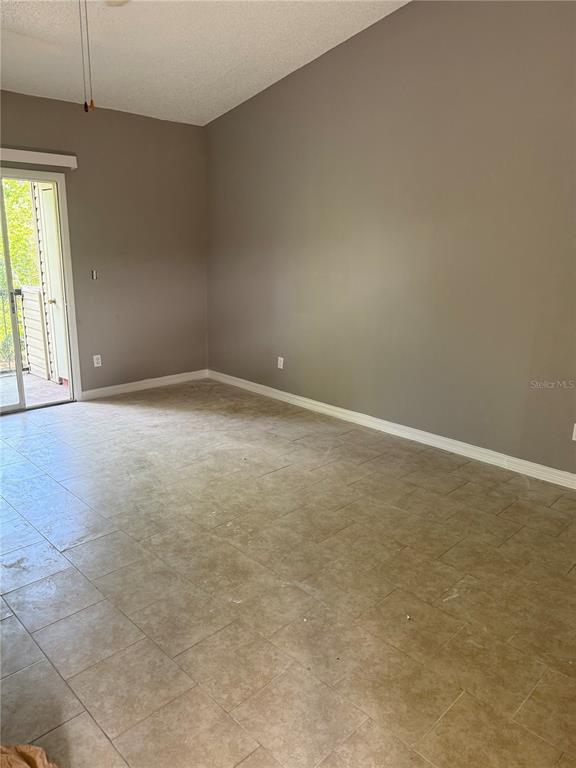 An empty room features beige tile flooring, gray walls, and a sliding glass door — 1948 LAKE ATRIUMS CIRCLE UNIT 133, ORLANDO, FL