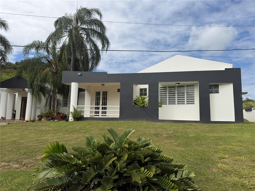 A single-story house with a dark gray exterior, white trim, and a large front lawn — 16 TRINITARIA, GURABO, PR