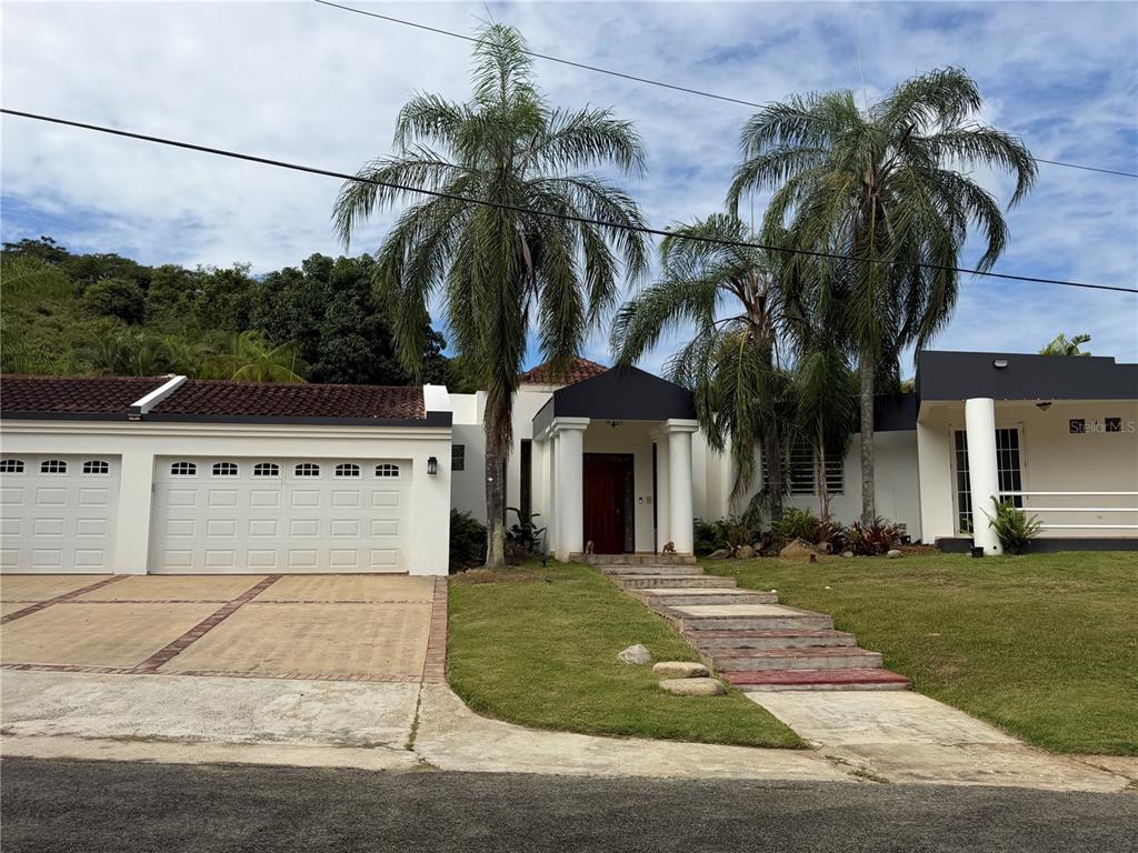 A single-story house with a two-car garage, palm trees, and a stepped walkway — 16 TRINITARIA, GURABO, PR
