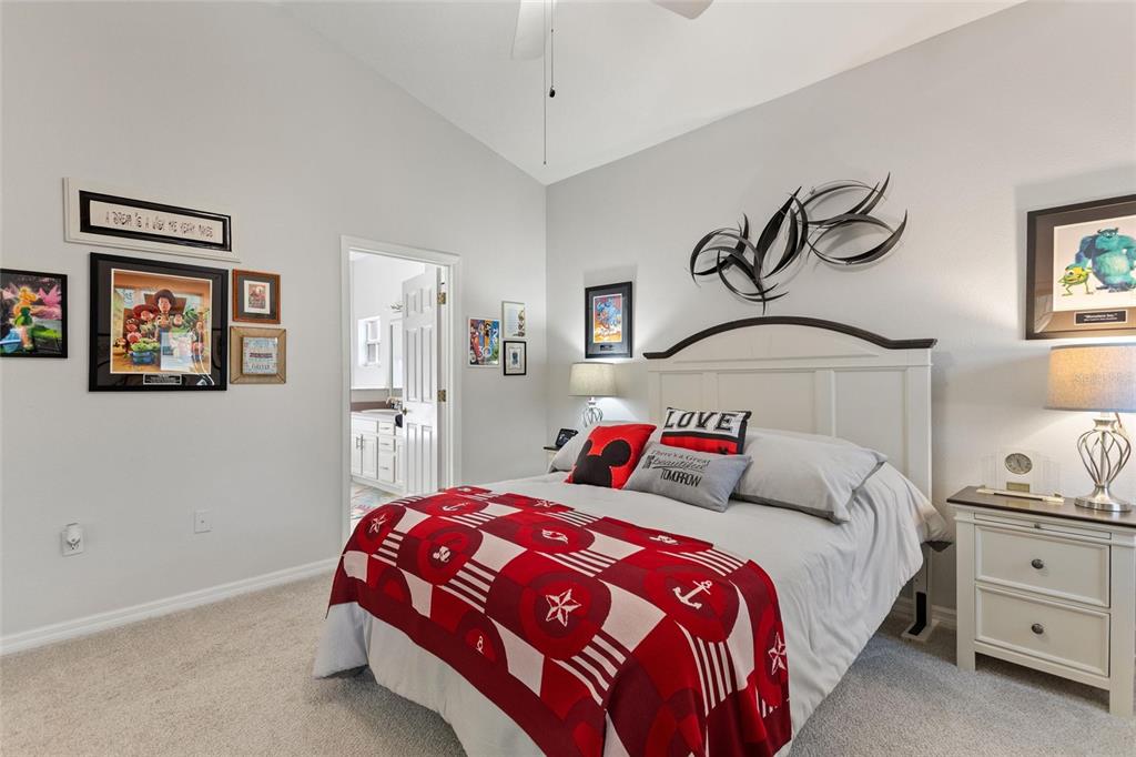 A bedroom features a white bed with a red patterned throw, wall art, and nightstands — 215 FITZGERALD LN, DAVENPORT, FL