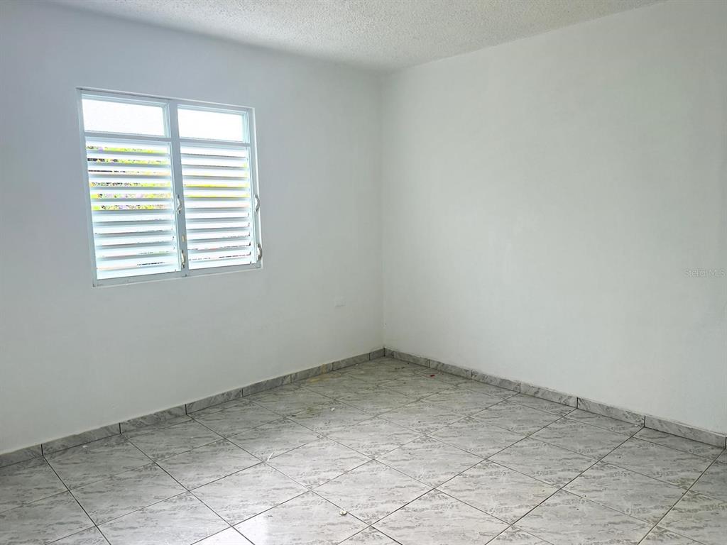 An empty room features white walls, a louvered window, and light-colored tiled flooring — 763 SAN SALVADOR, CAGUAS, PR
