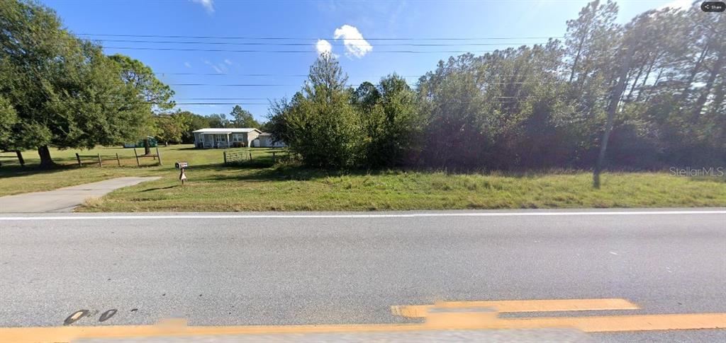 A single-story house sits behind a grassy lot next to a paved road — OLD GRADE RD, POLK CITY, FL
