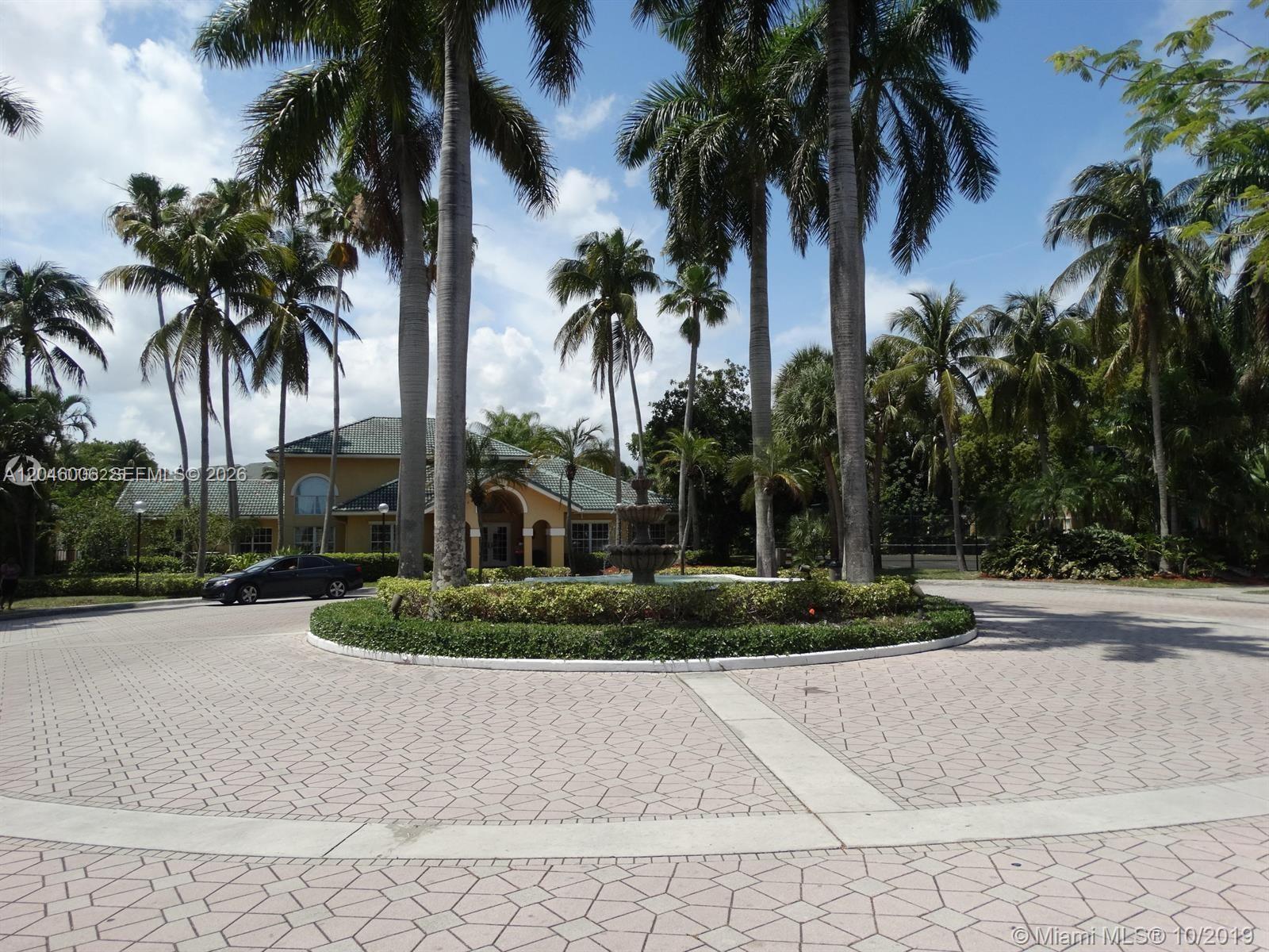 A circular driveway with a central fountain and palm trees leads to a suburban house — 4015 W Mcnab Rd # D210, Pompano Beach FL 33069, POMPANO BEACH, FL