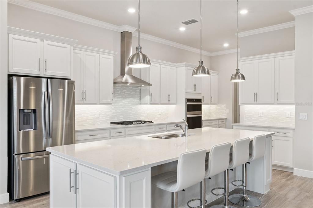 A modern kitchen features white cabinetry, a large quartz island, stainless steel appliances, and pendant lighting — 2745 NATURE VIEW ROAD, ST CLOUD, FL