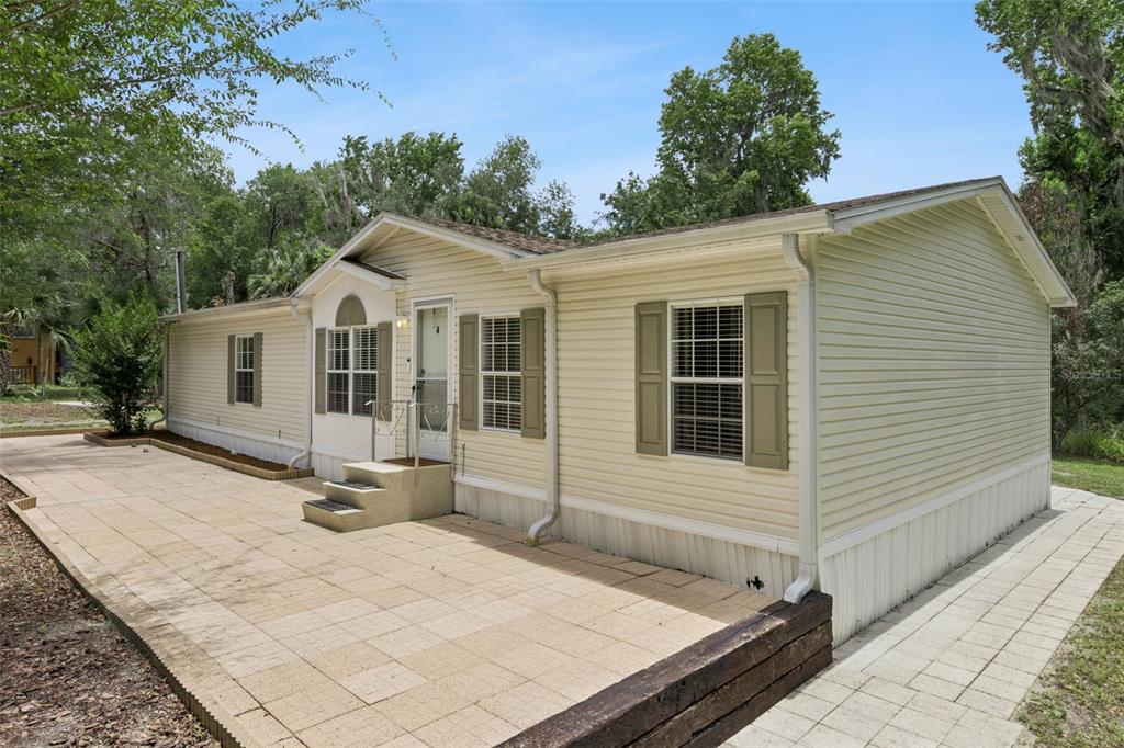 A light-colored mobile home with tan shutters and a large paved patio area — 16250 HAMILTON DR, ORLANDO, FL