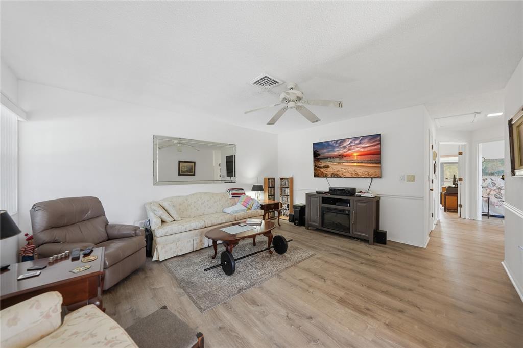 A living room features light wood flooring, a beige sofa, a TV, and a ceiling fan — 9 QUAILS RUN BOULEVARD UNIT 12, ENGLEWOOD, FL