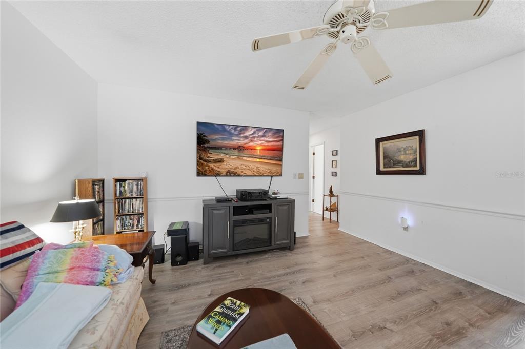 A living room features a wall-mounted television, a media console, and light wood-look flooring — 9 QUAILS RUN BOULEVARD UNIT 12, ENGLEWOOD, FL