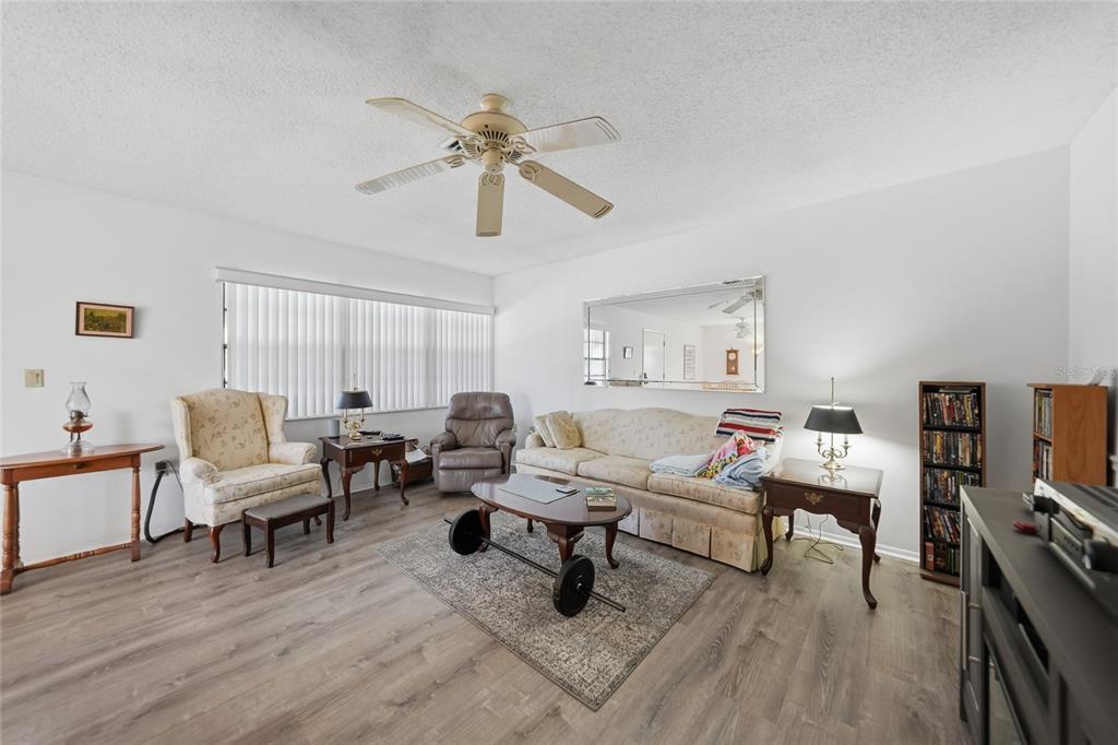 A living room features light wood-look flooring, a ceiling fan, a sofa, and armchairs — 9 QUAILS RUN BOULEVARD UNIT 12, ENGLEWOOD, FL