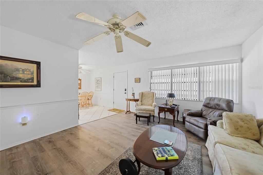 A living room features wood-look flooring, a ceiling fan, and a view into the dining area — 9 QUAILS RUN BOULEVARD UNIT 12, ENGLEWOOD, FL